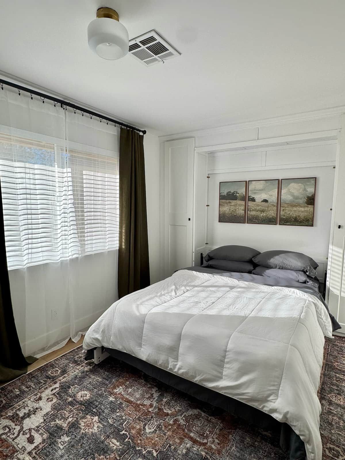 Un dormitorio con cama, una ventana con cortinas, un radiador y un cuadro colgado en la pared.