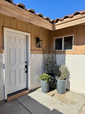 Une maison avec une porte blanche, une fenêtre et deux plantes en pot.