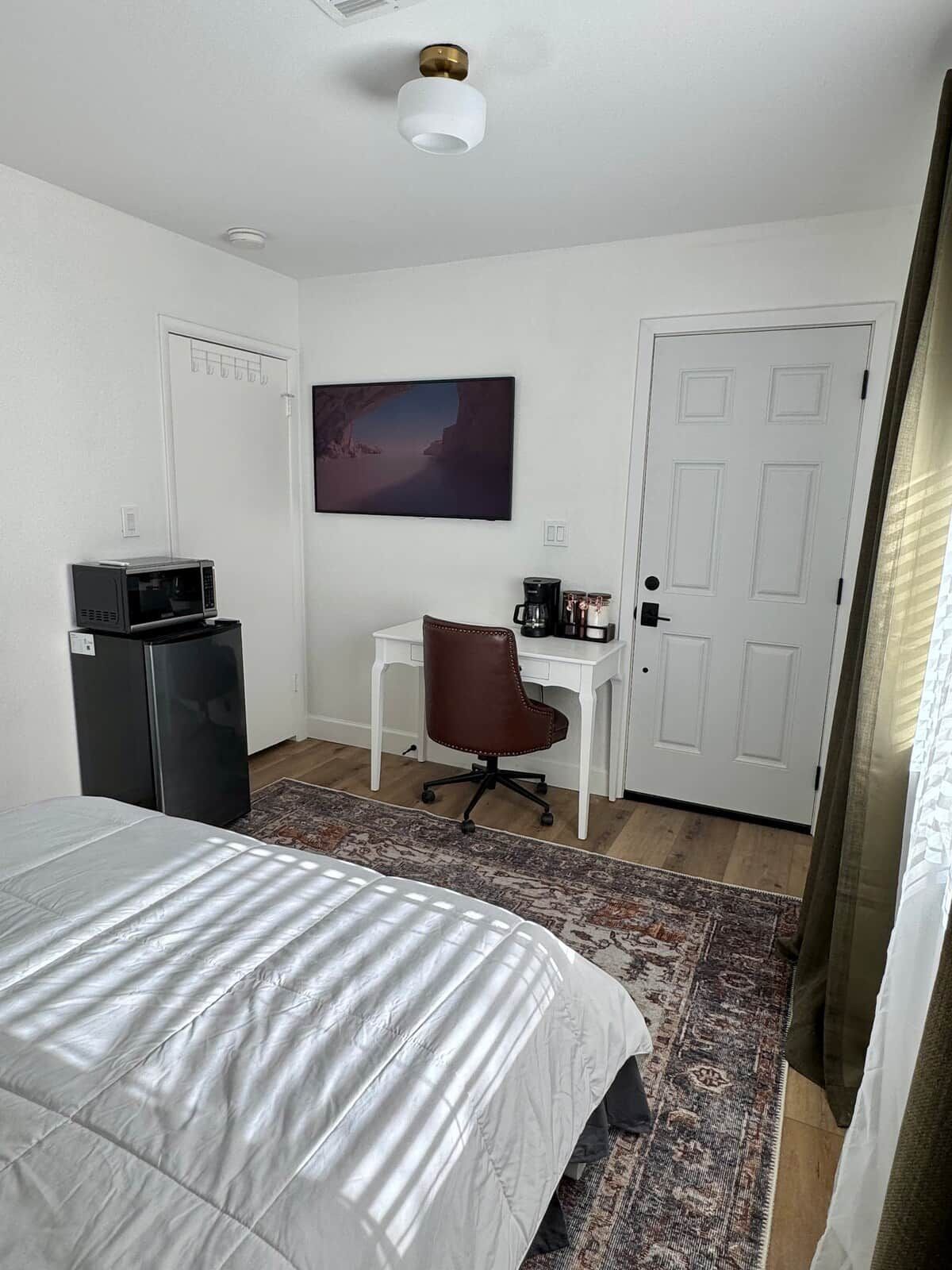 Un dormitorio con cama, escritorio, silla, microondas, cafetera y un cuadro en la pared.