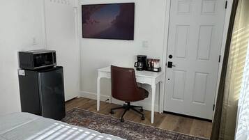 Un dormitorio con cama, escritorio, silla, microondas, cafetera y un cuadro en la pared.