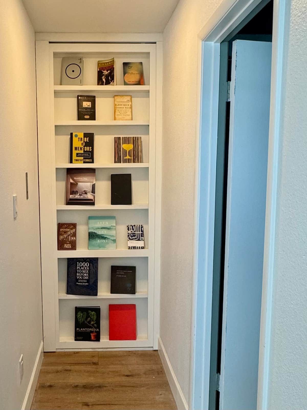 Un couloir étroit avec une bibliothèque blanche contenant divers livres et objets décoratifs.