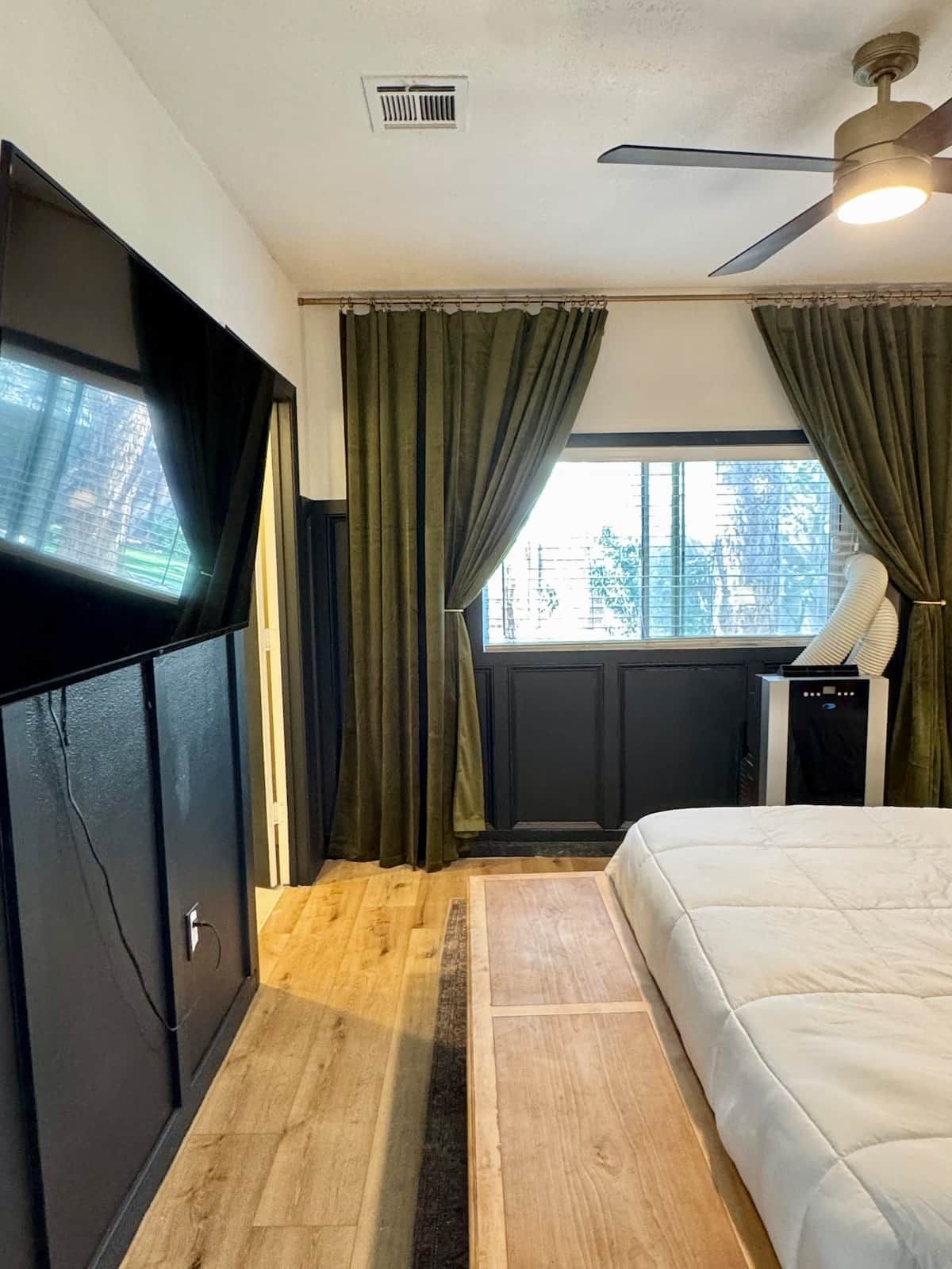 Un dormitorio con cama, televisor, calefactor y ventana con cortinas.