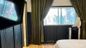 Un dormitorio con cama, televisor, calefactor y ventana con cortinas.