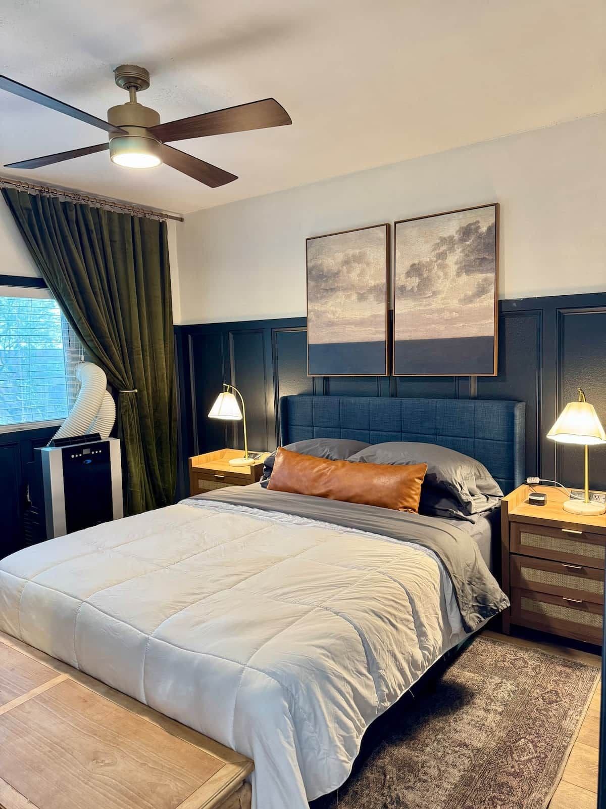 Une chambre à coucher avec un lit, des tables de chevet, un ventilateur de plafond et des œuvres d’art accrochées au mur.