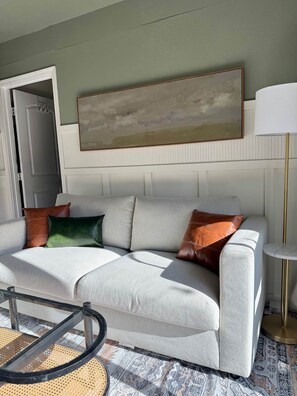 Een moderne woonkamer met een bank, een glazen salontafel en een schilderij aan de muur.