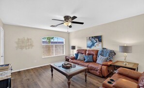 Ein Wohnzimmer mit einem Ledersofa, einem Couchtisch, einem Deckenventilator und einem Fenster mit Jalousien.