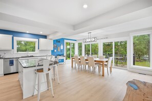 A modern kitchen with white cabinets, a blue accent wall, and a dining area with a wooden table and chairs.