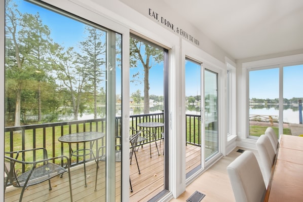A balcony with a view of a lake, furnished with tables and chairs, and a sign above reading 'EAT, DRINK, & ENJOY THE VIEW'.
