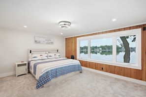 A bedroom with a large window, a bed with a blue and white checkered bedspread, a nightstand, and a wall-mounted artwork.