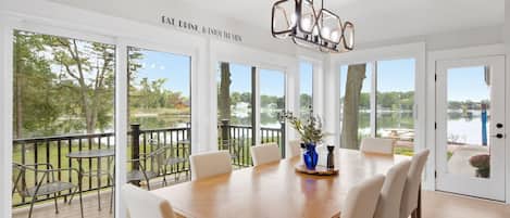 A dining area with a large table, chairs, and a view of a lake through large windows.