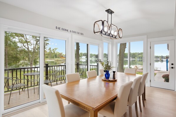 A dining area with a large table, chairs, and a view of a lake through large windows.