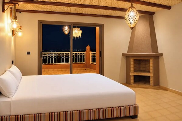 A bedroom with a large bed, a fireplace, and a balcony with a railing. - Riad Ouirgane Panorama (Ouirgane)