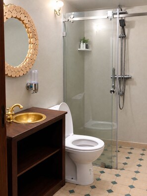 Un baño con lavamanos dorado, inodoro blanco y cabina de ducha con mampara de vidrio.
