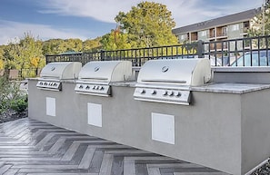 An outdoor barbecue area with three grills, a wooden deck, and a view of a residential building in the background.