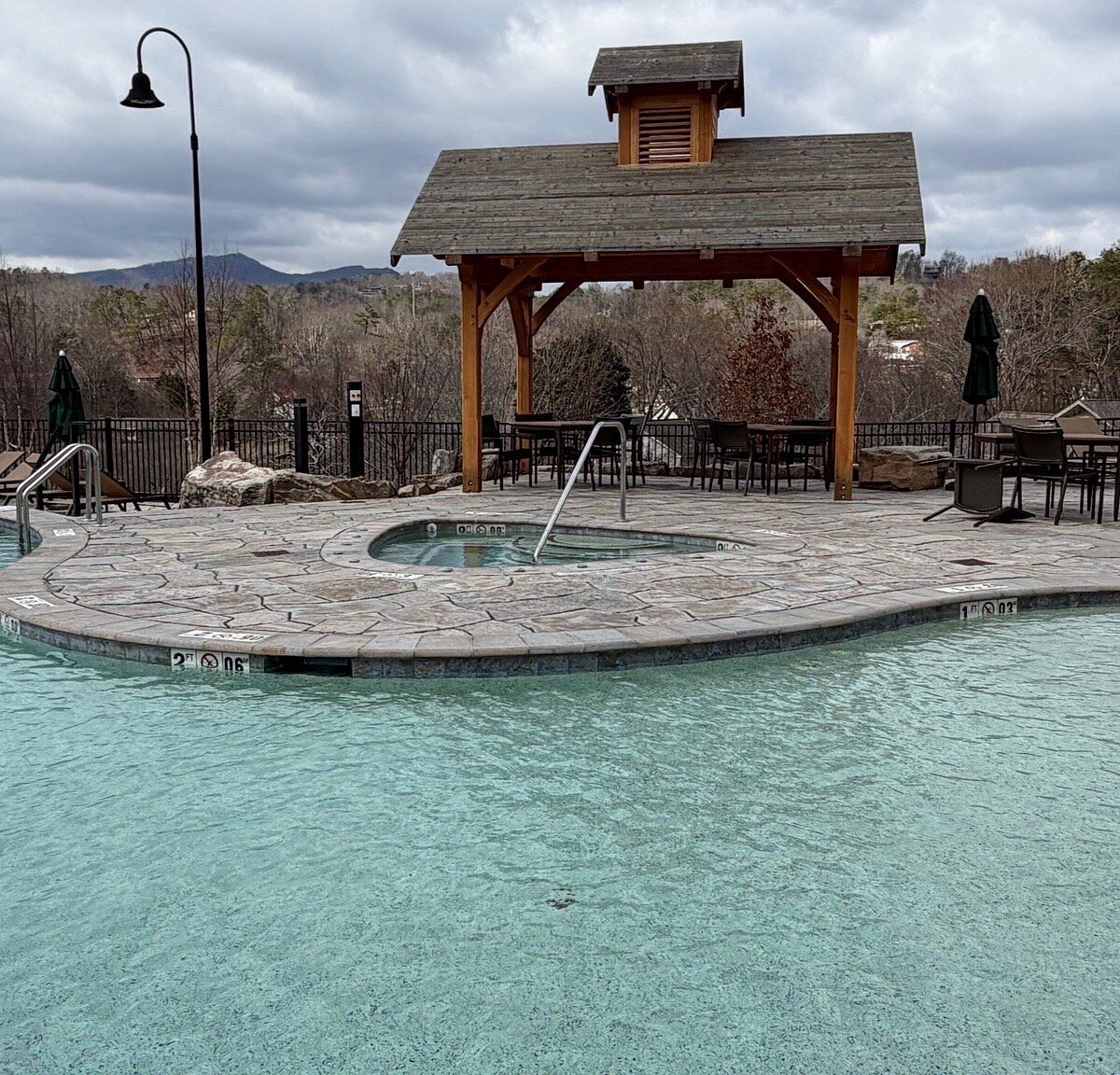 A pool area with a wooden gazebo, lounge chairs, and a hot tub.