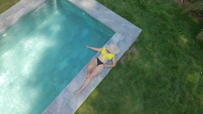 A person sitting by a rectangular pool with a stone edge, surrounded by a grassy area. - Apartamentos y Villas D Angelo - Superior Apartment 101 (Manzanillo)