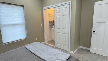 A bedroom with a bed, a ceiling fan, a closet, and a window with blinds.