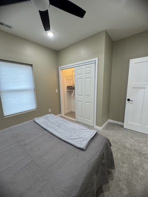 A bedroom with a bed, a ceiling fan, a closet, and a window with blinds.