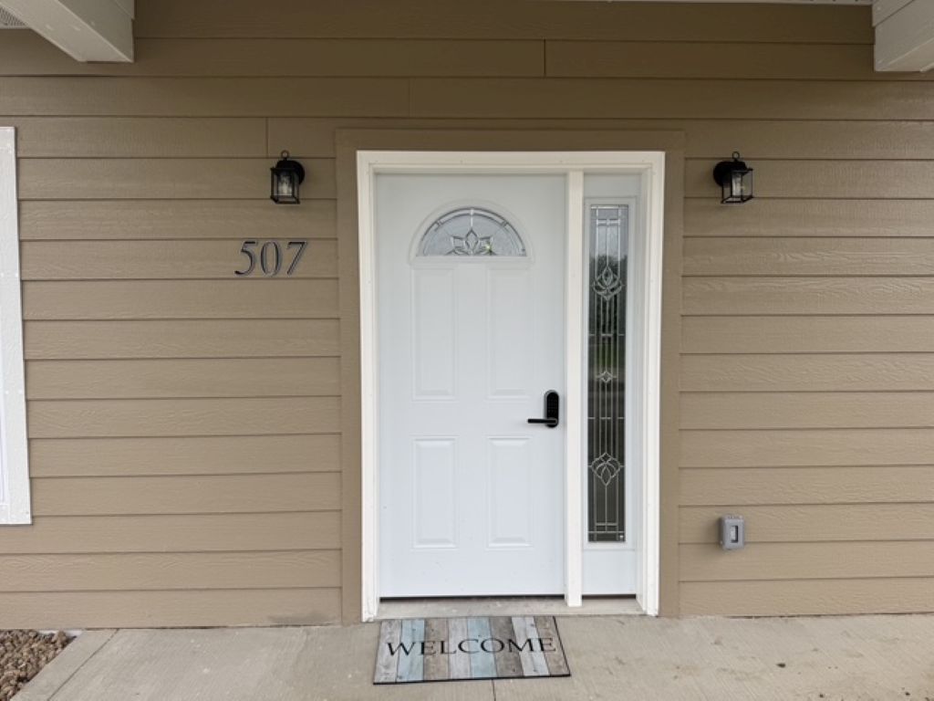 A beige house with a white door, number 507, and two wall-mounted lanterns.