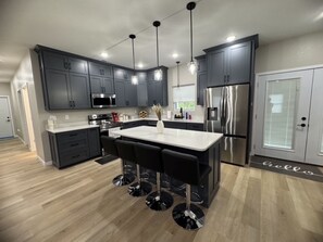 Una cocina moderna con armarios oscuros, electrodomésticos de acero inoxidable y una isla central con taburetes de bar.