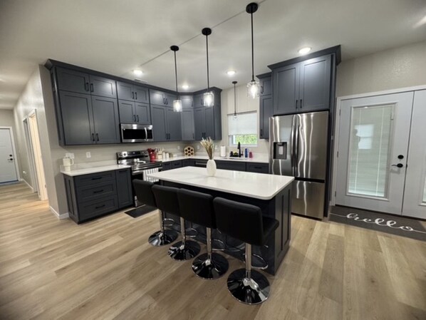 A modern kitchen with dark cabinets, stainless steel appliances, and a central island with bar stools.