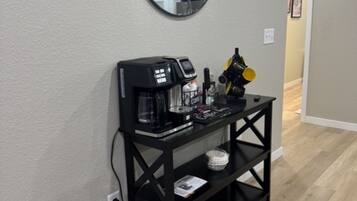 A black console table with a coffee machine, a small bowl, and a decorative item against a wall with a round mirror above it.
