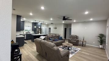 A modern living room with a sectional sofa, a coffee table, and a dining area with a kitchen in the background.