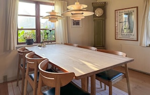 A dining area with a long wooden table, six chairs, a chandelier, a clock, and a poster on the wall. - 3 bedroom amazing home in Fanø (Fanø)