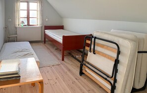 A room with a wooden floor, a bed with a red headboard, a small table with books, a window with curtains, and a radiator. - 3 bedroom amazing home in Fanø (Fanø)