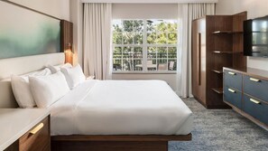 Habitación de hotel con una cama grande, un armario de madera, un televisor y una ventana con vistas a zonas verdes.