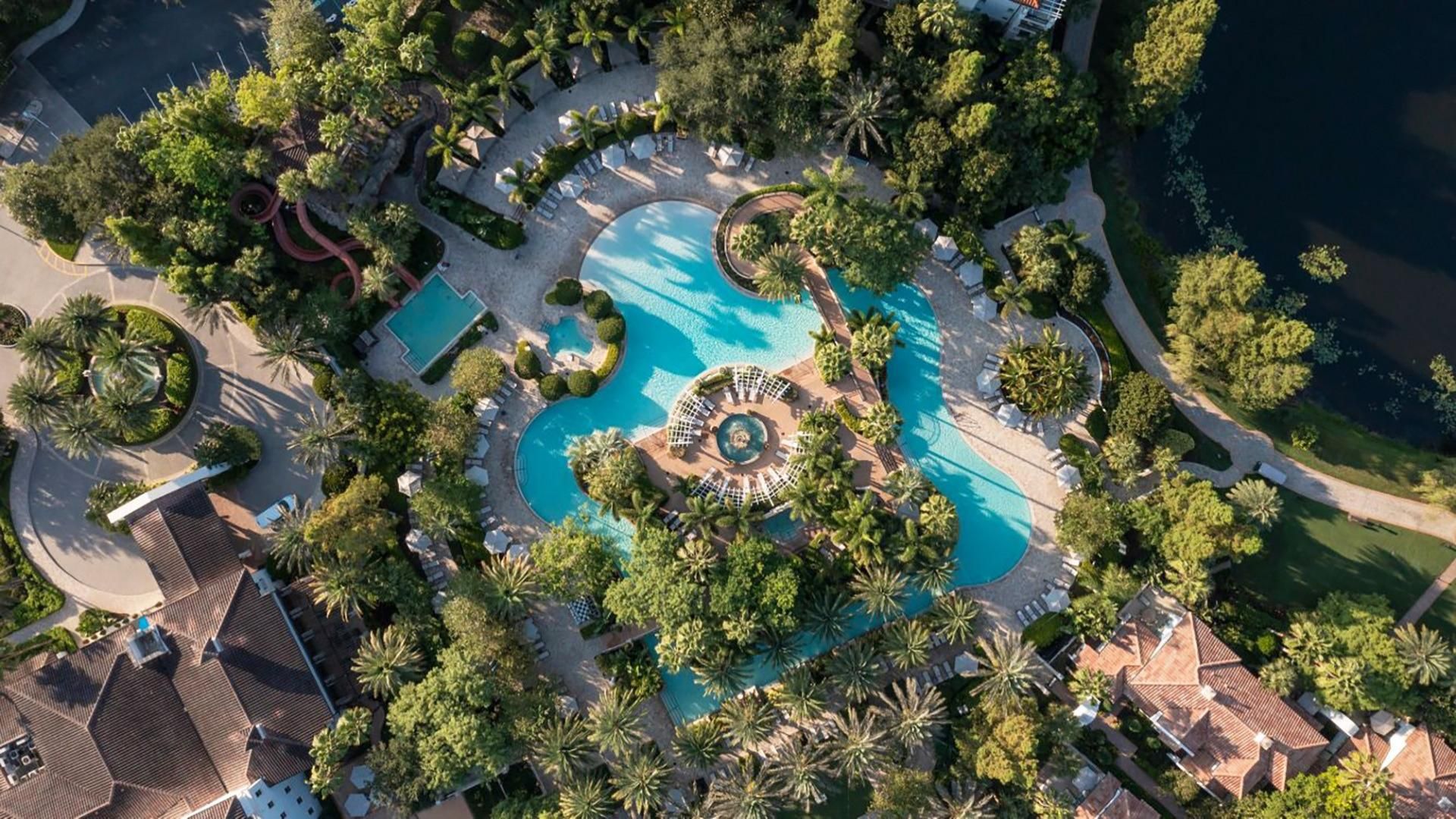 An aerial view of a resort with multiple swimming pools, palm trees, and a central fountain.