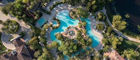 An aerial view of a resort with multiple swimming pools, palm trees, and a central fountain.