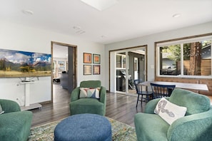 A spacious living area with a large flat-screen TV, a dining table with chairs, and a cozy seating area with green upholstered chairs and a blue ottoman. - Hot tub - Fireplace - Game Room (Flagstaff)