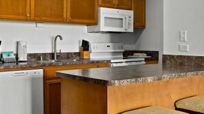 A kitchen with wooden cabinets, a microwave, a stove, a dishwasher, and granite countertops. - 2BR Suite at WorldMark Kapaa Shore on Kauai's Beautiful Coconut Coast (Kapaʻa)