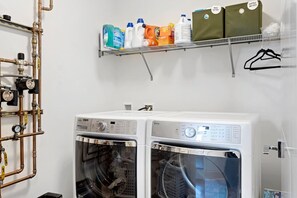 A laundry room with two front-loading washing machines, a metal shelf with detergent bottles, and a wall-mounted pipe system. - Modern 3 br townhouse near downtown (Seattle)