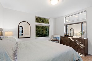 A bedroom with a large bed, a dresser, a mirror, and two windows with views of greenery. - Modern 3 br townhouse near downtown (Seattle)