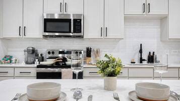 Una cocina moderna con armarios blancos, un microondas de acero inoxidable y una isla central con dos tazones y una planta en maceta.