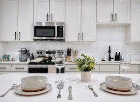Una cocina moderna con armarios blancos, un microondas de acero inoxidable y una isla central con dos tazones y una planta en maceta.