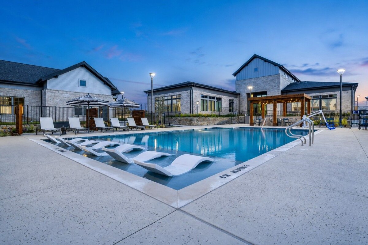 Una piscina con sillones de descanso, una zona de estar cubierta y un edificio con fachada de piedra.