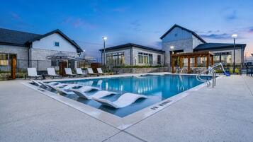 A swimming pool with lounge chairs, a covered seating area, and a building with a stone facade.