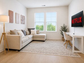 A modern living room with a sofa, a desk, a lamp, and a TV displaying 'NETFLIX'.