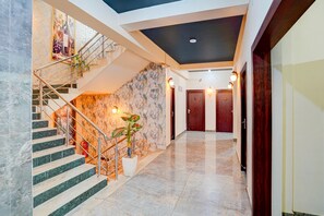 Un hall d’hôtel avec un escalier en marbre, une plante fixée au mur et un plafond doté d’un éclairage encastré.