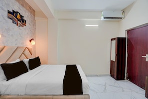 Une chambre d’hôtel avec un lit, un climatiseur fixé au mur, une table de chevet avec une lampe et un grand miroir.