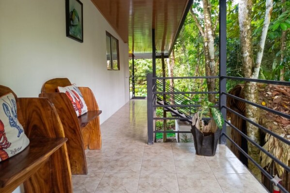 A reception area with wooden benches, a staircase leading to a balcony, and a view of a lush garden. - Apartamentos y Villas D Angelo - Junior Suite 108 (Manzanillo)