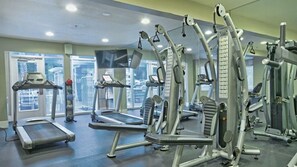 Une salle de sport équipée de machines de cardio, de postes d’entraînement avec poids et d’un tapis de course.