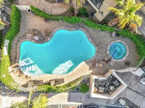 Una piscina de diseño curvo, rodeada por una terraza pavimentada con asientos y un pequeño jacuzzi circular.