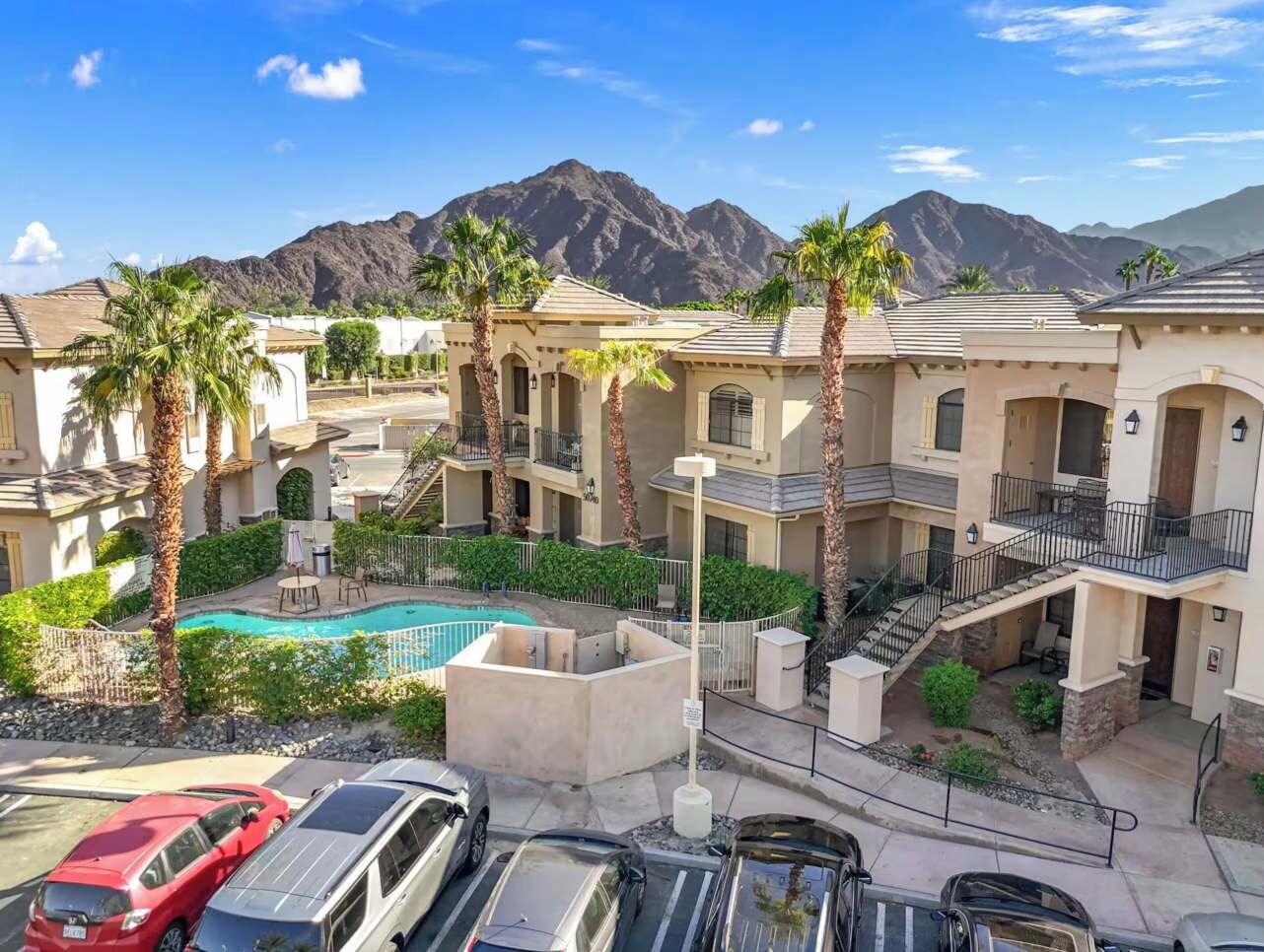 Un complejo residencial con piscina, palmeras y montañas al fondo.