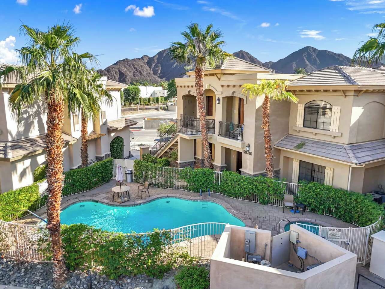 Zona de piscina con vista despejada a las montañas al fondo, rodeada de palmeras y un edificio con balcones.