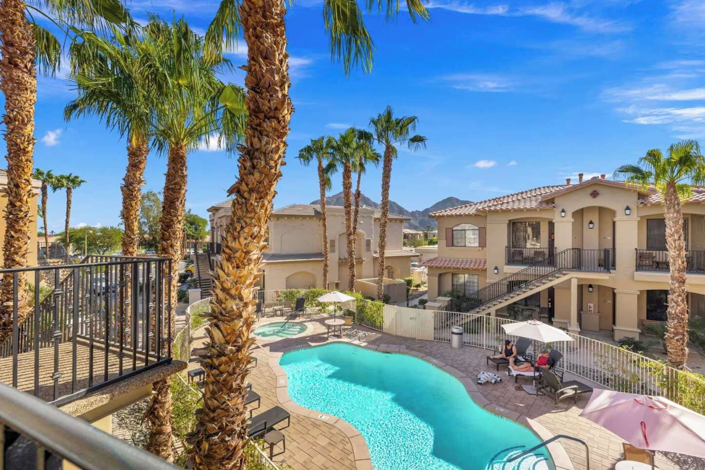 A pool area with palm trees, outdoor seating, and a building with multiple balconies.