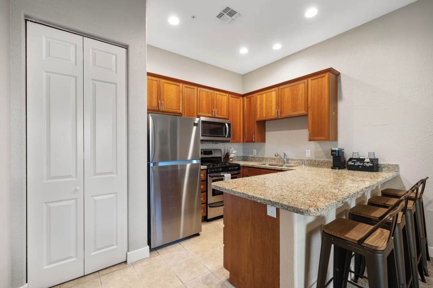 A kitchen with wooden cabinets, a stainless steel refrigerator, a microwave, and a granite countertop.